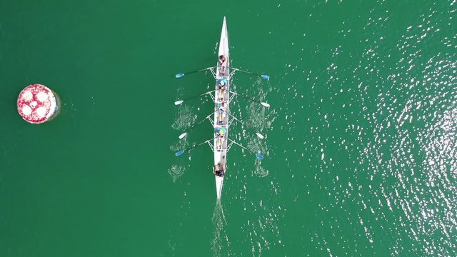 Aerial top down video of sport canoe operated by team of young men in emerald clear and calm lake waters