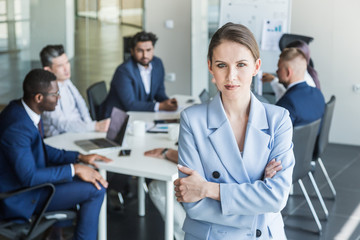 Business woman stands on the background of partners. A team of young businessmen working and communicating together in an office. Corporate businessteam and manager in a meeting