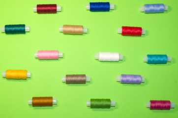 needlework, craft, sewing and tailoring concept - row of colorful thread spools on green background, flat lay, top view