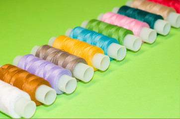 needlework, craft, sewing and tailoring concept - row of colorful thread spools on green background, flat lay, top view