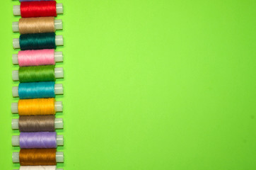 needlework, craft, sewing and tailoring concept - row of colorful thread spools on green background, flat lay, top view