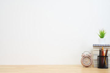 Office desk with alarm clock, pencil, plant vase and book stack.