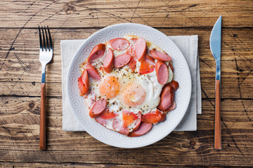 Fried eggs sausages and tomatoes on a plate on the table. Rich homemade Breakfast. Wooden background. Copy space.