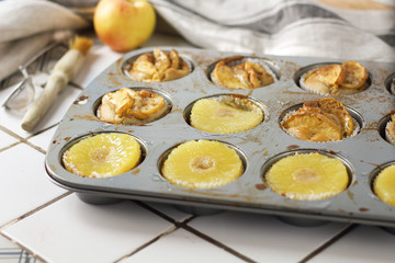 Muffins cupcakes with pineapple circles and apple slices in a cupcake muffin tray, on kitchen white tile near with pastry brush. Cake dessert photo for cook book recipe top view