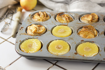 Muffins cupcakes with pineapple circles and apple slices in a cupcake muffin tray, on kitchen white tile near with pastry brush. Cake dessert photo for cook book recipe top view