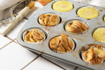 Muffins cupcakes with pineapple circles and apple slices in a cupcake muffin tray, on kitchen white tile near with pastry brush. Cake dessert photo for cook book recipe top view