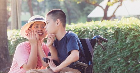 Obraz premium Disabled child on wheelchair and mom in the outdoor park, His mother sent love through the eyes and gentle hands touch, Life in the education age of special children, Happy disability kid concept.
