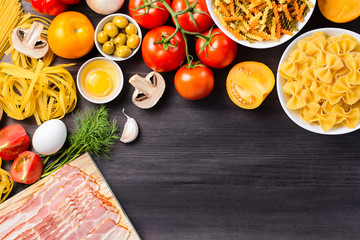 Italian food ingredients - pasta, vegetables, mushrooms, bacon, eggs, olives. Flat lay on dark wooden background