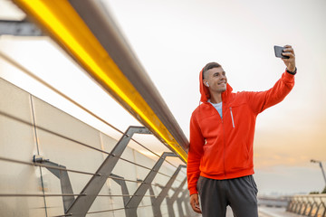 Contented Caucasian young sportsman taking selfies outdoors