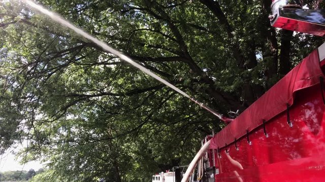 A red firetruck sprays a strong stream of water from its water cannon past trees