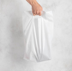 white plastic bag held by a woman's hand. light background.