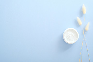 Natural cosmetic skincare moisturizer cream in jar and dry flowers over pastel blue background. Flat lay, top view, overhead. Skin care, beauty and healthcare concept.