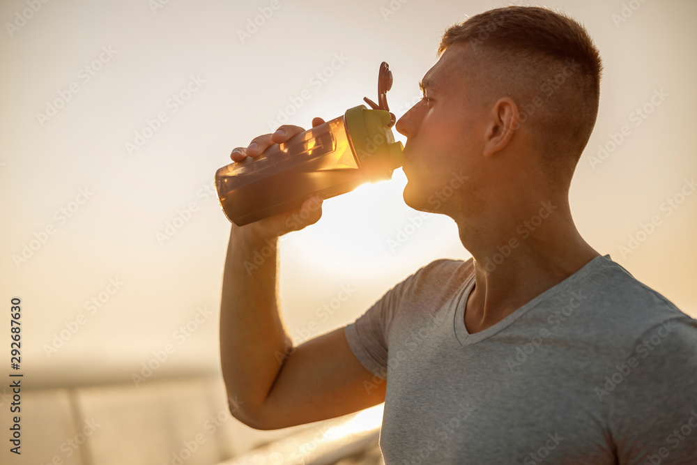 Wall mural good-looking young male athlete drinking water outdoors