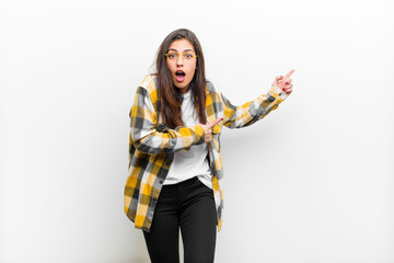 young pretty woman feeling shocked and surprised, pointing to copy space on the side with amazed, open-mouthed look isolated against white wall © kues1