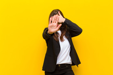 young  pretty woman covering face with hand and putting other hand up front to stop camera,...