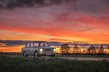 Obraz na płótnie Canvas Popular soviet time car in dramatic sunset. Colorful sky creates a picturesque atmosphere of a vintage, retro automobile on highway. 