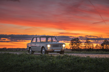 Fototapeta na wymiar Popular soviet time car in dramatic sunset. Colorful sky creates a picturesque atmosphere of a vintage, retro automobile on highway. 