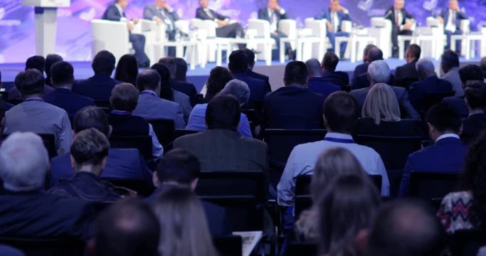 Politicians Or Scientists Speak From The Stage, People In Audience Sitting Back To The Camera. Spectators And Journalists At Scientific Or Political Press Conference, Briefing, View From Auditorium.