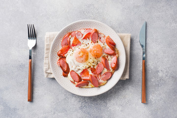 Fried eggs sausages and tomatoes on a plate on the table. Rich homemade Breakfast. Gray concrete background. Copy space.