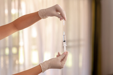 Hands in white medical latex gloves cover a syringe with a cap on a background of white curtains.Health concept. Healthy lifestyle concept. The concept of pharmacology