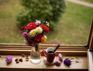 beautiful bouquet of asters and zinnias and a cup of hot drink on the windowsill against autumn...