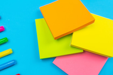 Photo of multi-colored bright felt-tip pens lying in the left corner on a blue background next to which is a set of multi-colored stickers of different colors. Close-up. Stationery.