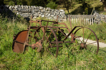 An old rusty piece of farm equipment lies abandoned in a Yorkshire Dales field and is gradually being overgrown with weeds