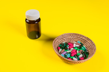 An empty brown jar with a closed white lid is located next to a wicker basket with pills and capsules.Health concept. 