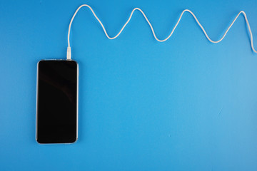 Wave shape of white cable attached on smartphone over blue background