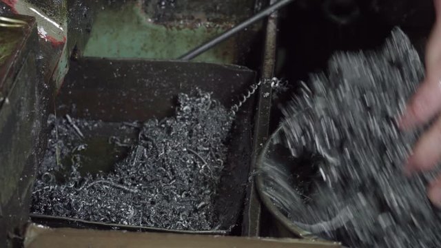 working engineer in the factory, removes metal shavings with his hands from the compartment into the trash.