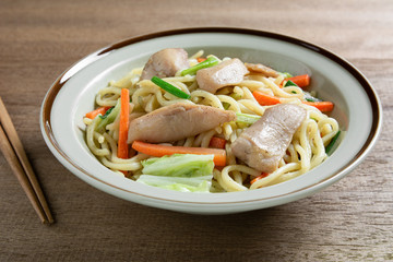 close up of stir fried japanese noodles with chicken and vegetables in a ceramic dish on wooden table. asian homemade style food concept.