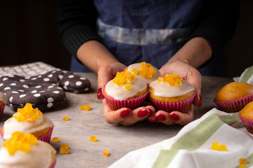 Confectioner' s female hands holding the citrus muffins. Fresh muffins on a confectionery table