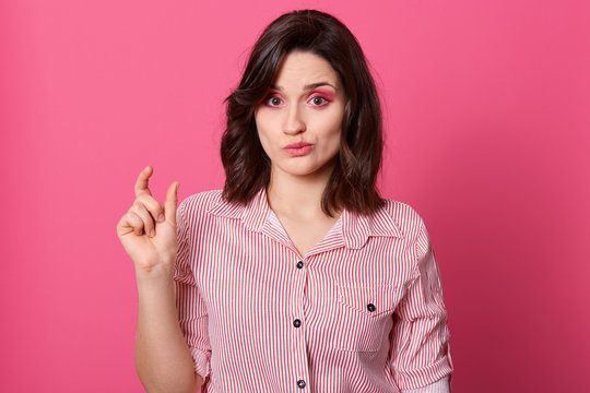 Half Length Portrait Of Woman Showing Small Amount Of Something And Having Sneering Facial Expression, Posing Isolated Over Rosy Background, Good Looking Lady Wearing Striped Shirt. People Concept.