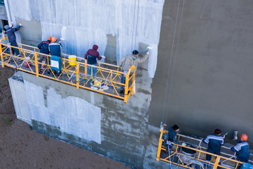 Along the wall of the high-rise building are two groups of builders in the facade lifts. One group...