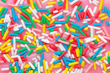 flat lay of colorful sprinkles on glaze pink background, top view