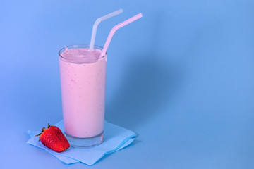 glass of pink strawberry milkshake or cocktail with berry on blue background