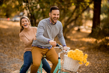 Active young couple enjoying together in riding bicycle in golden autumn park