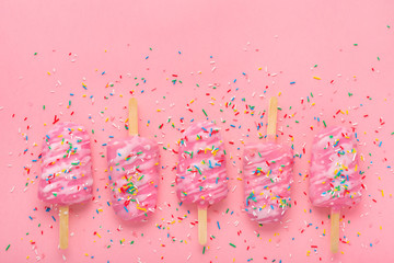 popsicle with sprinkles and icing on pink festive background with copy space