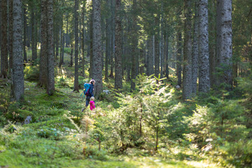 Hiker mother with backpack and daughter walking on path and exploring summer spruce forest. Enjoying the pristine nature.