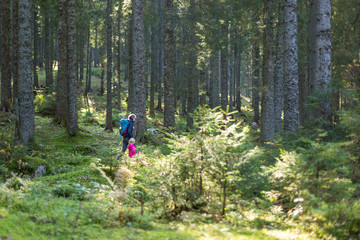 Obraz premium Hiker mother with backpack and daughter walking on path and exploring summer spruce forest. Enjoying the pristine nature.