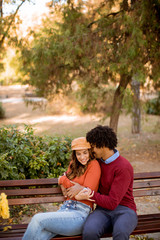 Fototapeta premium Multiratial loving couple sitting on bench in the autumn city park