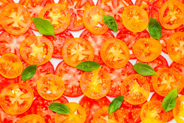 trendy pattern of sliced ripe red, yellow and orange tomatoes decorated green leaves of basil on white background, flat lay