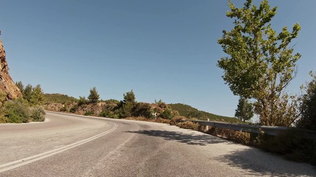 POV of a motorcyclist riding on a mountain road with bends on the Greek island of Thasos. Summer day, scenic road.