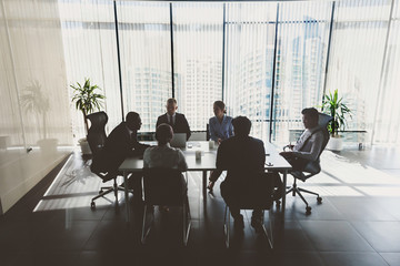 Silhouettes of people sitting at the table. A team of young businessmen working and communicating together in an office. Corporate businessteam and manager in a meeting
