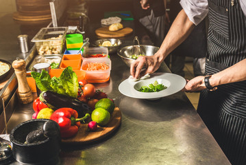 Professional chef cooking in the kitchen restaurant at the hotel, preparing dinner. A cook in an apron makes a salad of vegetables and pizza.