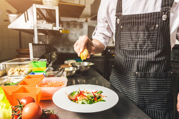 Professional chef cooking in the kitchen restaurant at the hotel, preparing dinner. A cook in an apron makes a salad of vegetables and pizza.