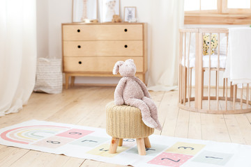 Scandinavian children's room: a basket for toys, a plush rabbit sitting on a chair, a cradle for a...