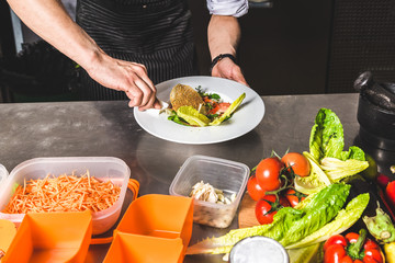 Professional chef cooking in the kitchen restaurant at the hotel, preparing dinner. A cook in an apron makes a salad of vegetables and pizza.