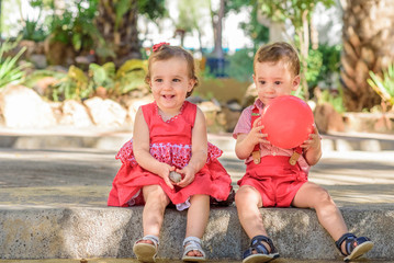 twin brother giving his sister a kiss on the cheek. Children playing in the park with a red balloon.