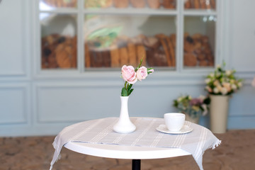 Coffee break. A cup of coffee in the morning in a cafe. Coffee cup and vase with flowers on the table against the background of a bakery showcase with buns. Cup of tea on the terrace on an autumn day